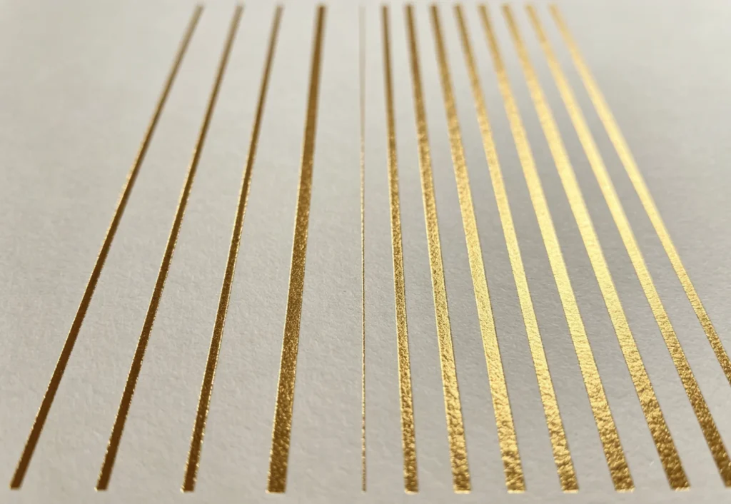 Gradated thin to thick solid gold foil stripe test on white paper to demonstrate minimum line width rules for brass hot stamping dies.