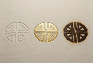 Direct side-by-side comparison of blind emboss, metallic gold foil, wood heat burn finishes with identical geometric logo on white paper.