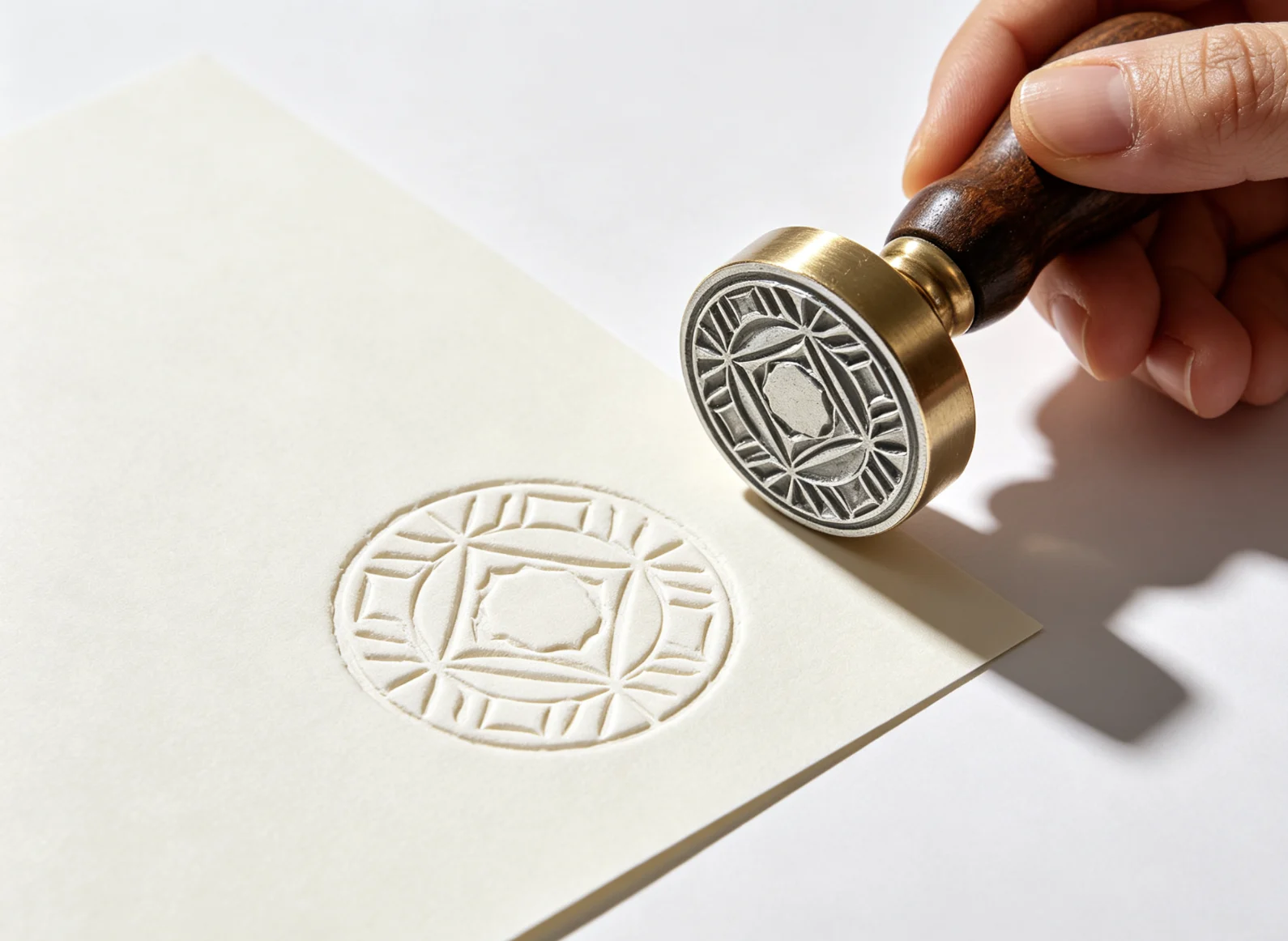 Hand holding ZHENGFEI matched steel emboss die seal beside crisp raised blind geometric round impression on smooth cream paper.