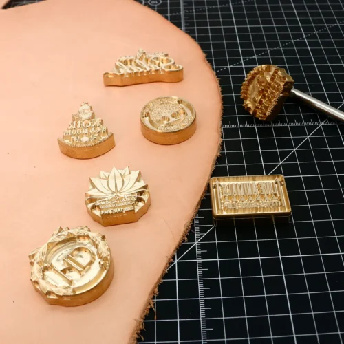 Lotus, wreath monogram custom brass stamp collection with matching branding iron head and machine fixture brass dies on leather grid mat.