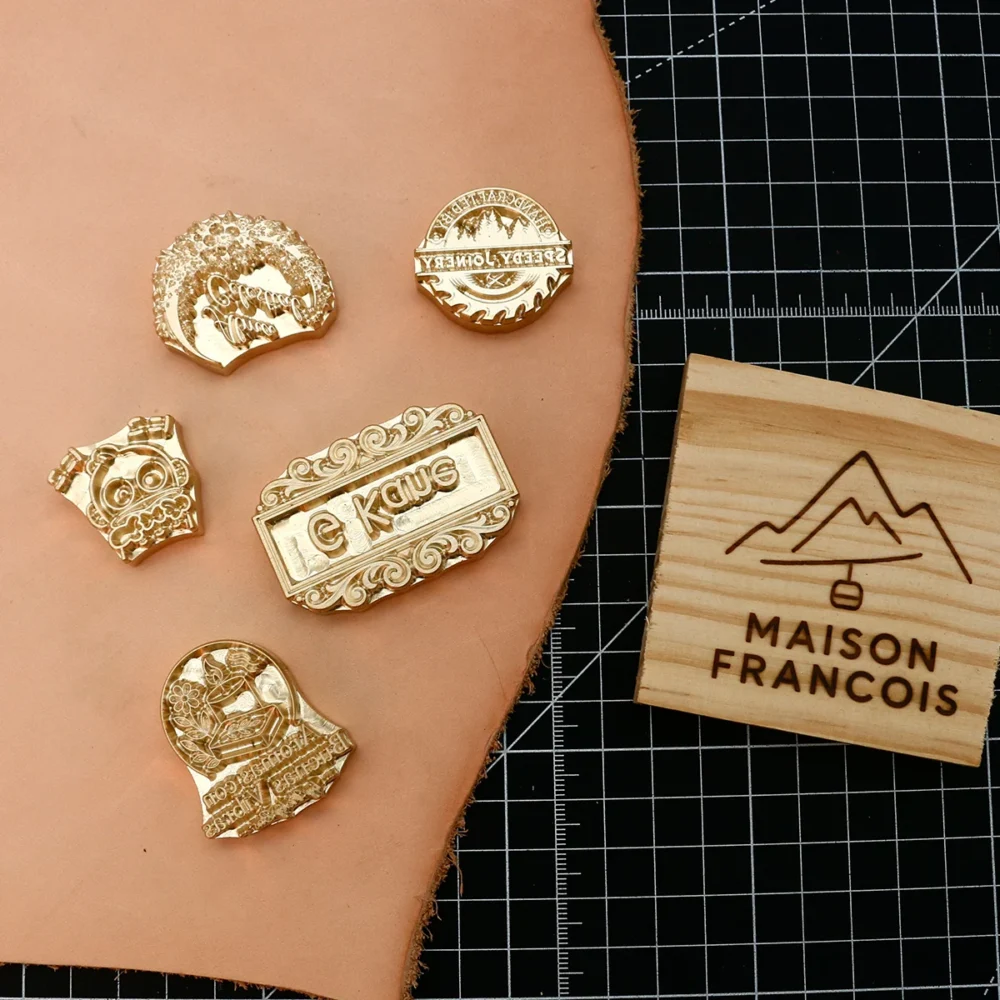 Cartoon graphic, ornate scroll rectangular brass logo stamps paired with branded wood slice sample on grid cutting mat.