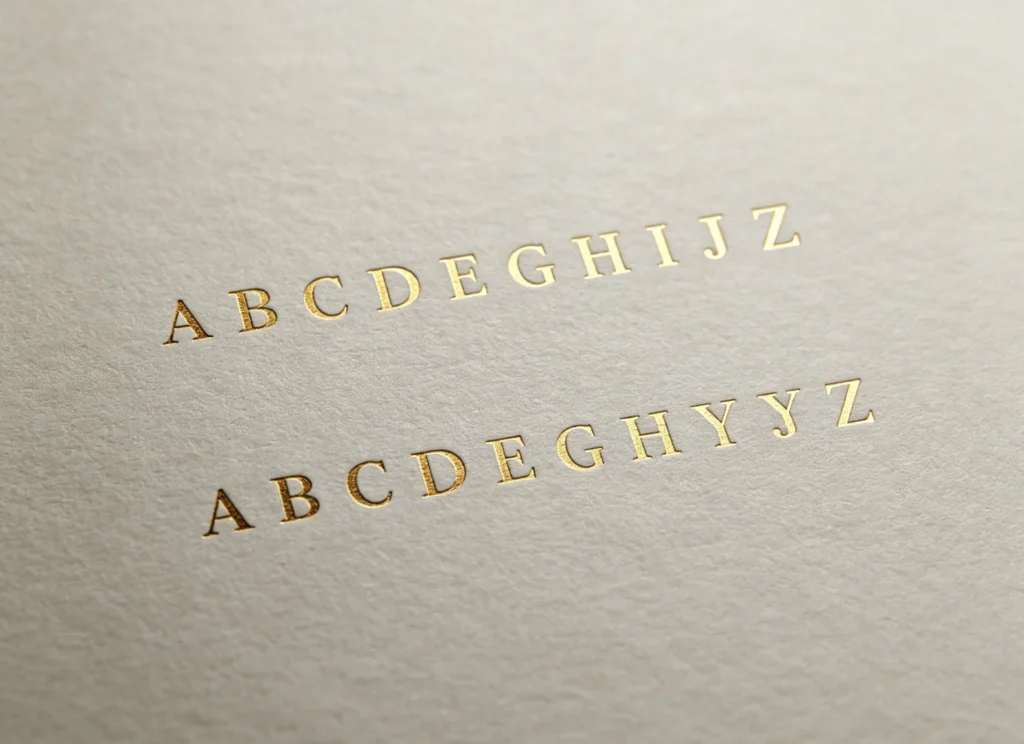 wo perfectly horizontal matching rows of gold foil alphabet stamped on cream paper with calibrated ZHENGFEI brass letter set & alignment jig.