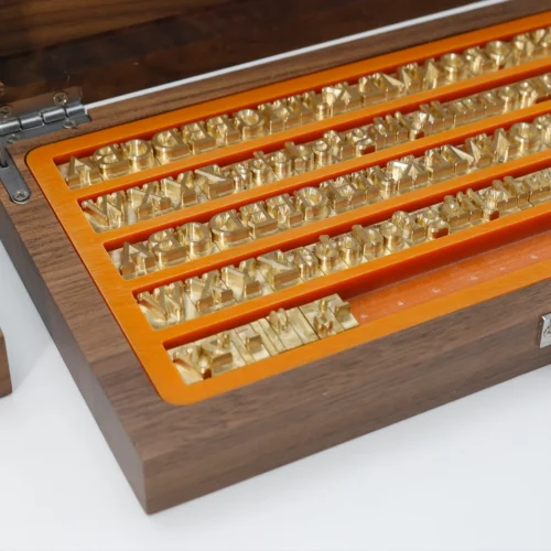 Close‑up of brass alphabet number stamps neatly arranged inside premium walnut wooden storage case