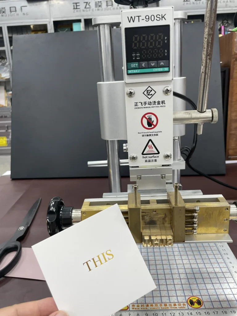 WT-90SK manual hot foil press stamping gold lettering onto glossy cardstock with a brass die
